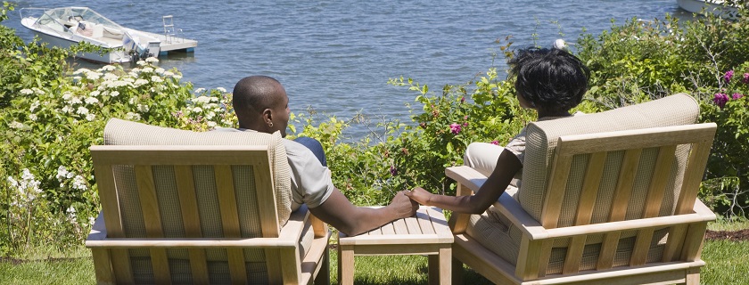 Un couple assis dans des chaises en bois se tient par la main, près d'un lac.