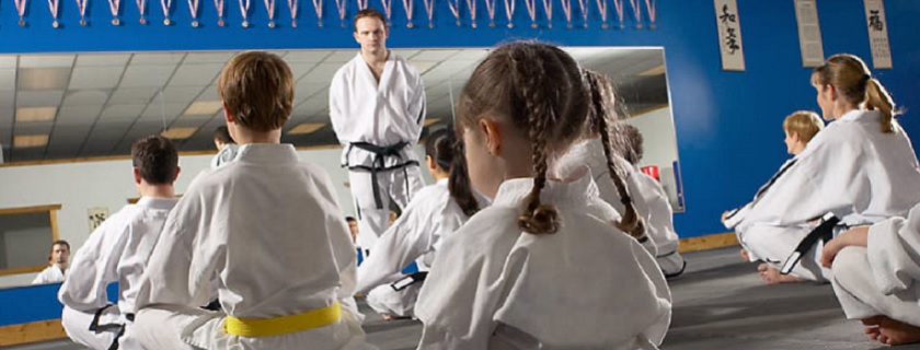 Neuf enfants assis, vêtus d'un uniforme blanc de karaté, qui regardent leur moniteur.